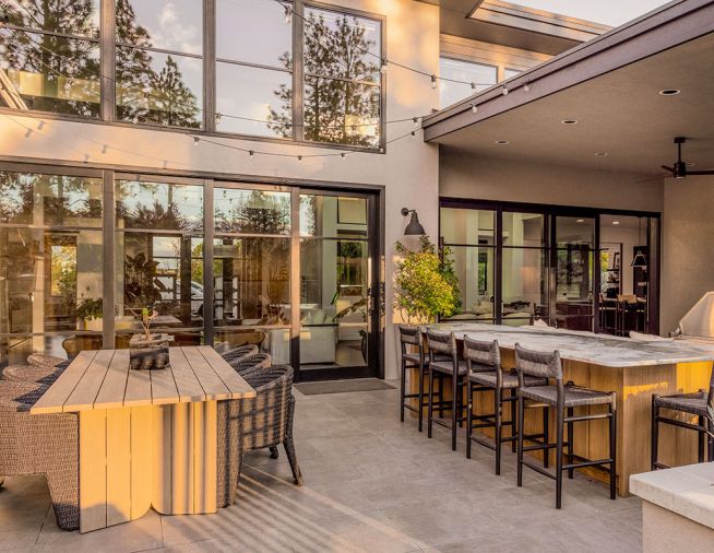 The dual dining area includes counter and table seating options from Area Rug Connection. A teak Four Hands Giorgio table and Fae dining chairs pair with Lomas outdoor counter stools in black teak under the leathered and weathered quartzite countertop.