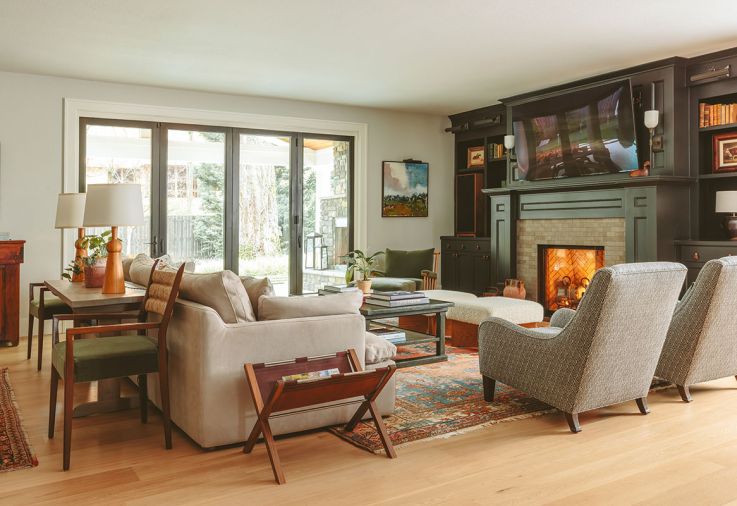Warm and comfy living room furnishings include Hollywood at Home Cole Armchairs and a Wicklow coffee table from Rose Tarlow Melrose House. Urban Electric Co. sconces distinguish the mantel and a Persian rug grounds the room.