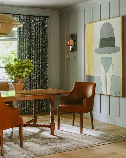 Michelle Russo artwork pops against the gray board and batten wall. To enhance the moody space, Humphrey chose a patterned Fortuny curtain fabric, letting the walnut table and chairs become the showstopper. An antique rug from Mehraban Rugs provides a soft surface underneath.