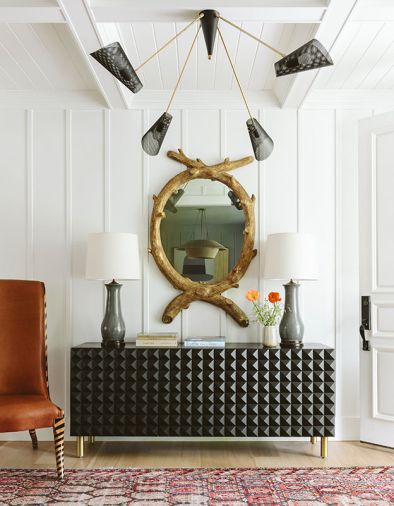 An eclectic combination of unique finds creates a showstopping entry. Set against a tongue and groove coffered ceiling, a black Lawson-Fenning chandelier teams with a geometric Sabin sideboard. A &ldquo;had-to-have&rdquo; Grisaille side chair counters the 22-carat shellacked tree mirror.