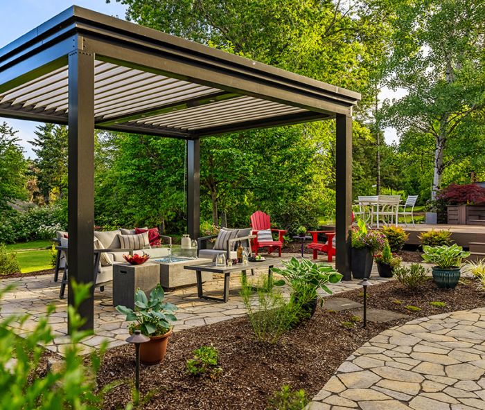 The freestanding louvered pergola in &ldquo;Onyx&rdquo; from The Luxury Pergola adds year-round protection to seating area and firepit which sits on top of Panorama Flag pavers. The lighting along the pathway adds dimension at night.