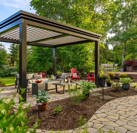 The freestanding louvered pergola in &ldquo;Onyx&rdquo; from The Luxury Pergola adds year-round protection to seating area and firepit which sits on top of Panorama Flag pavers. The lighting along the pathway adds dimension at night.