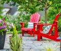 A pair of red Adirondack chairs add a pop of color to the transition between the existing deck and the eye-catching seating area with a fire feature. Candy-striped Petunias fill an upright urn.