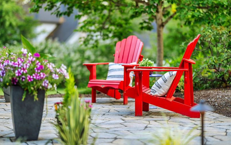 A pair of red Adirondack chairs add a pop of color to the transition between the existing deck and the eye-catching seating area with a fire feature. Candy-striped Petunias fill an upright urn.