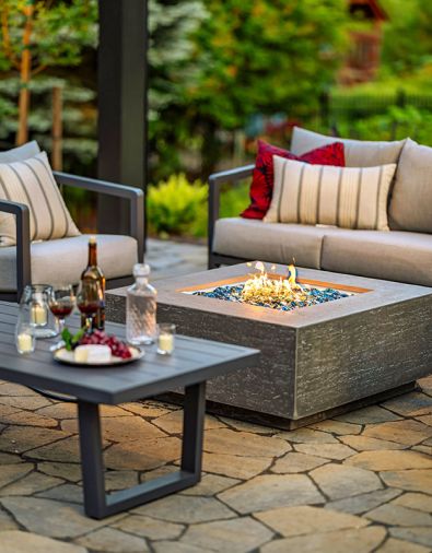 A cozy evening gathering is held around the fire feature as the intimate space glows beneath the pergola. The area adjoins a 3-piece patio wicker bar set from Avawing.