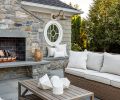 Another seating area offers a warm, inviting retreat centered around an outdoor fireplace. A pair of Kingsley Bate sofas, accented with custom pillows and paired with a slatted coffee table, create a comfortable yet polished setting for relaxed gatherings and effortless entertaining.