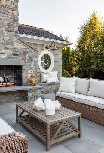 Another seating area offers a warm, inviting retreat centered around an outdoor fireplace. A pair of Kingsley Bate sofas, accented with custom pillows and paired with a slatted coffee table, create a comfortable yet polished setting for relaxed gatherings and effortless entertaining.