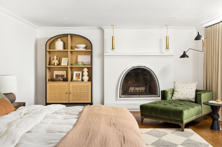In the bedroom, a diamond-patterned Loloi rug works well against a green velvet chaise. The fireplace, which was redone in plaster, is now a standout element in the space, infusing warmth and style in chillier months.
