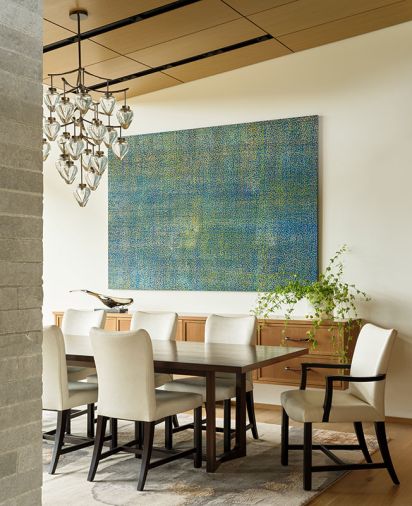 The dining room hosts a custom table across from Howardena Pindell artwork. The blown glass chandelier by Holly Hunt and Alison Berger Glassworks replicates the look of blooms on a branch.