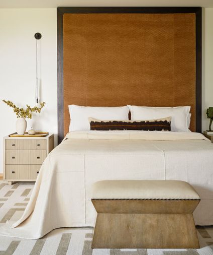 In the primary bedroom, an elegant bench at the end of a bedframe with custom headboard.