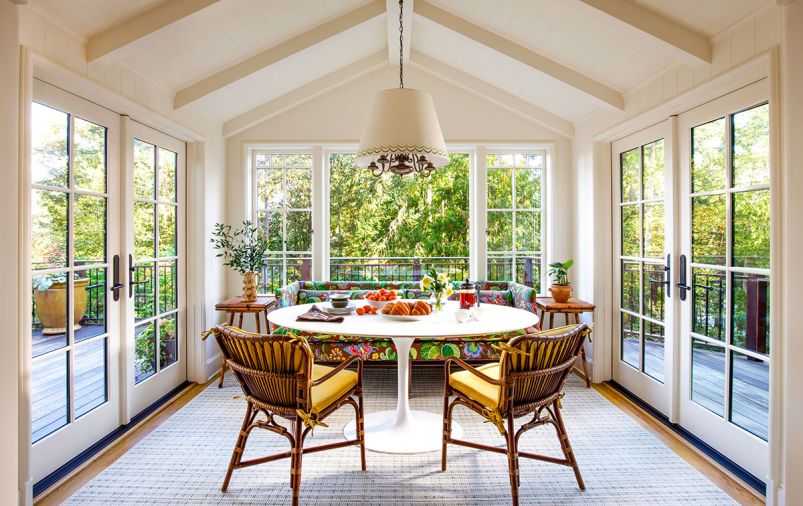 In the rebuilt breakfast room, Jessica Lane Interiors paired a custom sofa in Josef Frank&rsquo;s &ldquo;Exotic Butterfly&rdquo; fabric with a Saarinen-style table and retro rattan chairs with custom cushions. The vintage chandelier is from Hippo Hardware with a shade painted by Lonesome Pictopia.