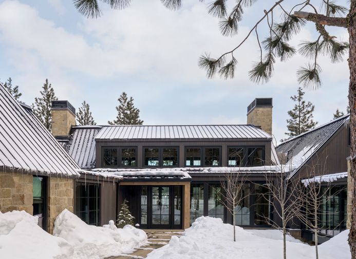 The exterior is covered in neutral sandstone from Select Stone, juxtaposed to the dark siding. A standing seam metal roof protects from harsh weather and prevents deep snow from accumulating on top of the home. Bisom Landscape Architecture LLC helped create a welcoming entrance and designed the surrounding landscape.