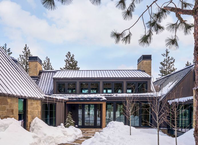The exterior is covered in neutral sandstone from Select Stone, juxtaposed to the dark siding. A standing seam metal roof protects from harsh weather and prevents deep snow from accumulating on top of the home. Bisom Landscape Architecture LLC helped create a welcoming entrance and designed the surrounding landscape.