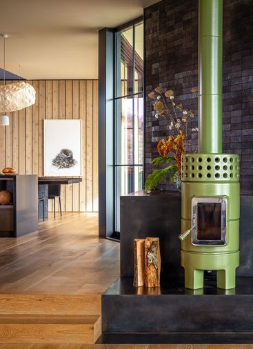 In the living room, the La Castellamonte Roundstack Slim stove in &ldquo;Verde&rdquo; is placed before a wall covered in &ldquo;Coal Creek&rdquo; clay bricks from Mutual Materials.