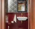 The powder bathroom is inviting and fun thanks to beaded paneling painted in &ldquo;Preference Red&rdquo; by Farrow & Ball and quirky cat-themed wallpaper from Divine Savages.