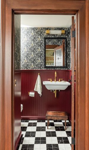 The powder bathroom is inviting and fun thanks to beaded paneling painted in &ldquo;Preference Red&rdquo; by Farrow & Ball and quirky cat-themed wallpaper from Divine Savages.