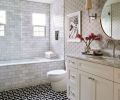 Guests enjoy the Sitka Whirlpool Bath from Mirabelle set against handsome Carrara White Tile from Daltile. Feather Fan &ldquo;Ecru&rdquo; wallpaper from Cole & Son evokes the 1930s style.