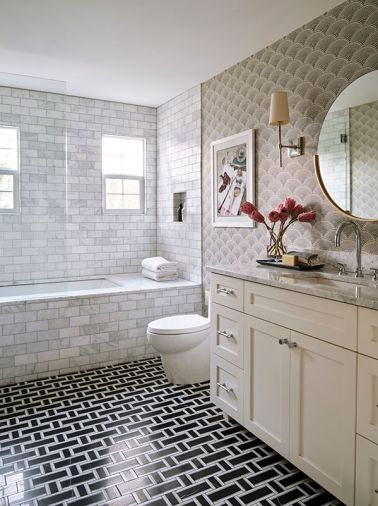 Guests enjoy the Sitka Whirlpool Bath from Mirabelle set against handsome Carrara White Tile from Daltile. Feather Fan &ldquo;Ecru&rdquo; wallpaper from Cole & Son evokes the 1930s style.