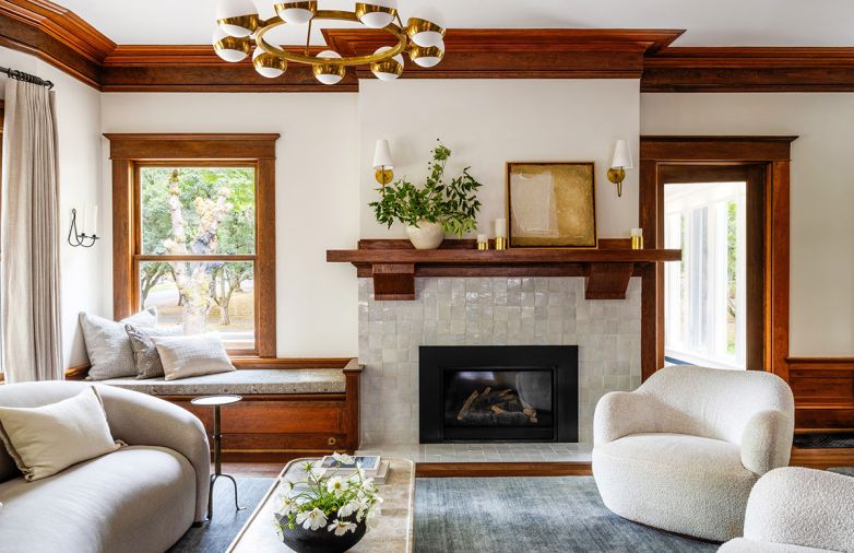 The carefully restored and artfully hewed Craftsman fireplace mantel is balanced with handmade tiles whose natural imperfections catch the light. A rounded Petra Natural Stone coffee table reiterates living room&rsquo;s curved furnishings. Restored original window woodwork pairs with a cozy window seat trimmed with custom Pindler fabric.
