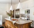 Conical handcrafted pendants by The Lamp Workshop brighten counters from Galaxy Stone Works Inc. Appliances from Eastbank Contractor Appliances are surrounded by oak cabinetry and an elegant tile backsplash from Cle Tile.