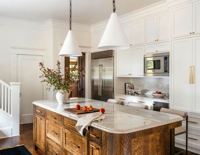 Conical handcrafted pendants by The Lamp Workshop brighten counters from Galaxy Stone Works Inc. Appliances from Eastbank Contractor Appliances are surrounded by oak cabinetry and an elegant tile backsplash from Cle Tile.