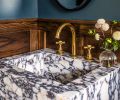 The powder room takes a step outside typical Craftsman style by adding a dramatic Calacatta Viola marble sink, paired with brass Waterworks fixtures. Reflective lighting and an oval mirror contrast with the intense wall color.