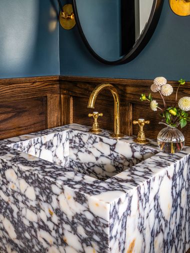 The powder room takes a step outside typical Craftsman style by adding a dramatic Calacatta Viola marble sink, paired with brass Waterworks fixtures. Reflective lighting and an oval mirror contrast with the intense wall color.