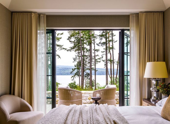 Lighter spaces like the primary bedroom are soft and breathable, offering a sense of calm and quiet expansion. The walls are covered in Apex Linen from Gregorius Pineo paired with custom bed and nightstands, and on the patio, woven swivel chairs from RH.