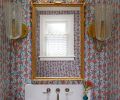 The powder room is trimmed in South African Watsonia Flower wallcovering by Pierre Frey. A gilded Grand Baroque mirror, Kohler sink and faucet, as well as custom vanity and cabinetry dress the room.