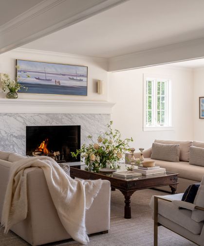 A refinished living room fireplace features Bianco Carrara marble from Stratus Surfaces and the sofas are from Restoration Hardware. The coffee table is fashioned from an antique Indian inlaid brass door.