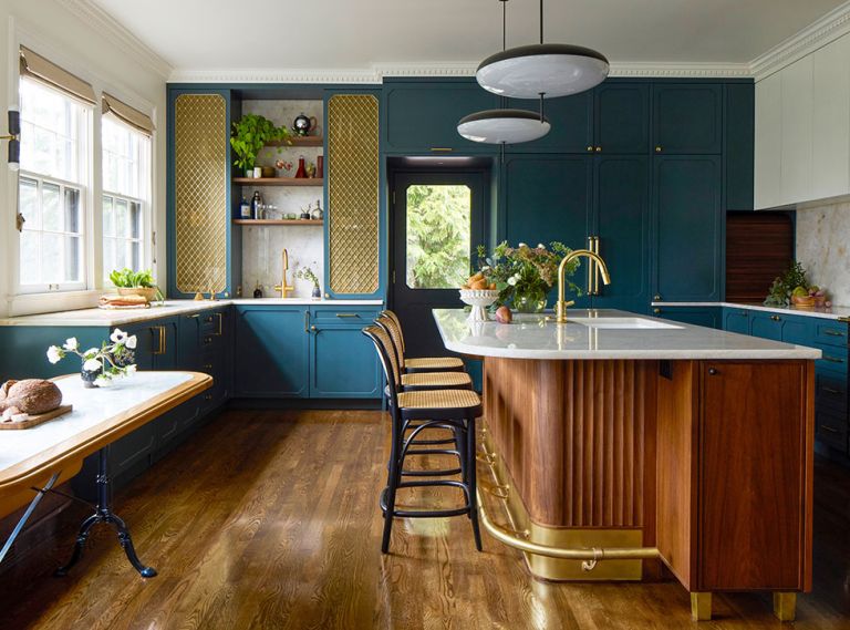 The custom cabinetry throughout the kitchen is designed by Bright Designlab, built by Master Furniture Makers, and painted in &ldquo;Vanderberg Blue&rdquo; from Benjamin Moore. The bespoke island has a quartzite counter, fluted details, brass accents, and is lit by Gino Sarfatti pendants.