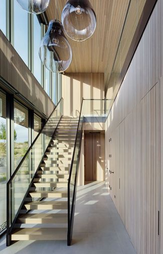 The two-story entry features a sweeping staircase with a Skywall railing system and cedar risers that echo the cedar ceiling. On the right, doors lead to a closet, powder room and bedrooms.