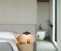 ABOVE The primary bedroom includes a custom bed with headboard in &ldquo;Nitty Witty&rdquo; fabric from Perennial. Lit floating bedside tables add to the calming ambiance. A view into the bathroom includes the Essentia, Bain Ultra soaking tub.