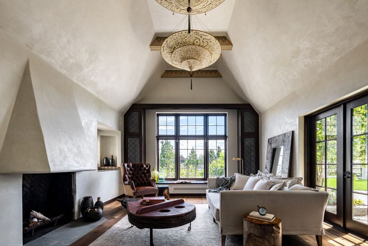 The living room was one of the beautiful original spaces the team wanted to preserve. The interior plasterwork was painted &ldquo;Floral White&rdquo; from Benjamin Moore, while the fireplace has a custom stucco surround. From the ceiling hangs a Scheherazade 3 Tiers Herbarium Silk Lamp from Fortuny.