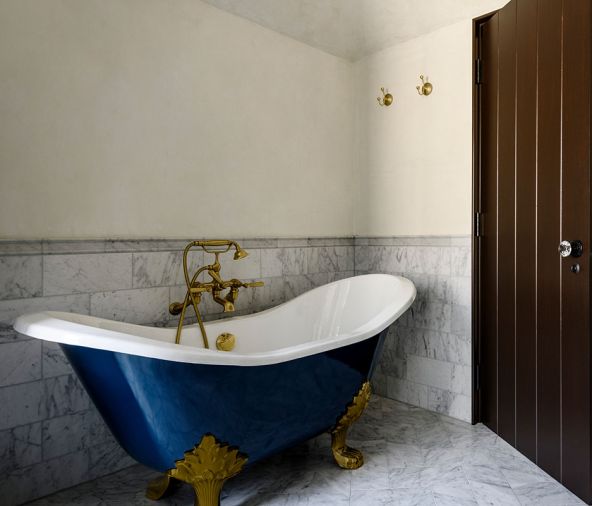 In the primary bathroom, the freestanding tub was painted &ldquo;Washington Blue&rdquo; from Benjamin Moore and has a Waterworks bath filler in aged brass from Rejuvenation.