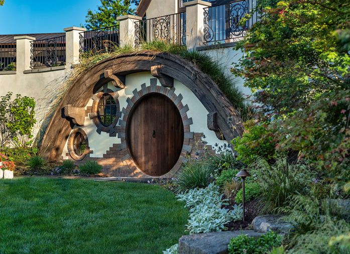 The Hobbit door is a delight for all who find it. The custom pivot door was designed and crafted by Thomas Fragnoli Construction. It&rsquo;s surrounded by concrete made to look like a curved wooden timber, with tufts of grasses tucked around it.
