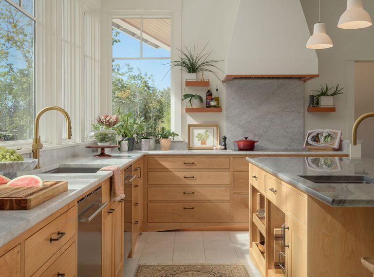 The light and airy kitchen gives a cheerful vibe even on overcast days, with a tactile palette of alder cabinetry, Carrara marble, and Kohler brass fixtures from Ferguson Home. Maple hardwood flooring in the adjoining space reiterates the wood tones in the kitchen.