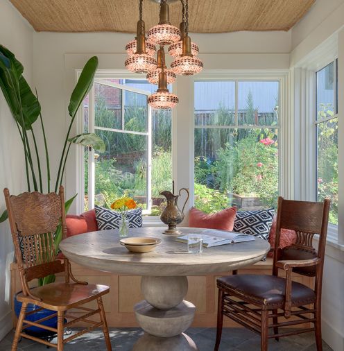 The sunroom, which looks out into the back garden, has a custom jute rug on the ceiling for sound dampening, a Turkish pendant light, antique chairs, and a stone table from Anthropologie.
