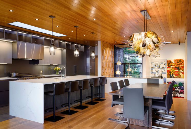 The kitchen has custom-tailored, sustainable Italian cabinets from Pedini NW in a Moka finish, with Misterio Gold quartz counters from Architectural Surfaces. The dining room includes a salvaged local walnut tree table from Urban Hardwood with a blown glass chandelier made by artist Julie Conway.
