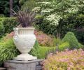 The low hedge separating swaths of lawn use two colors of boxwood for a festooned effect, similar to ironwork on the house. Golden Japanese forest grass softens harsh edges and corners, and pink spirea provides a burst of long-blooming color.