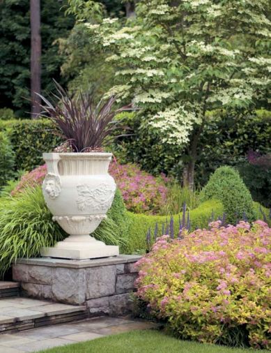 The low hedge separating swaths of lawn use two colors of boxwood for a festooned effect, similar to ironwork on the house. Golden Japanese forest grass softens harsh edges and corners, and pink spirea provides a burst of long-blooming color.