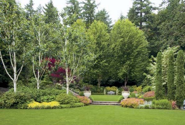 Jacquemontii birches with stark white trunks see their color mirrored in stone urns that flank broad stone steps from the upper to the lower lawn abutting the lakeshore. Another trio of trees, this time columnar Italian cypress, provide a formal contrast to the birches.