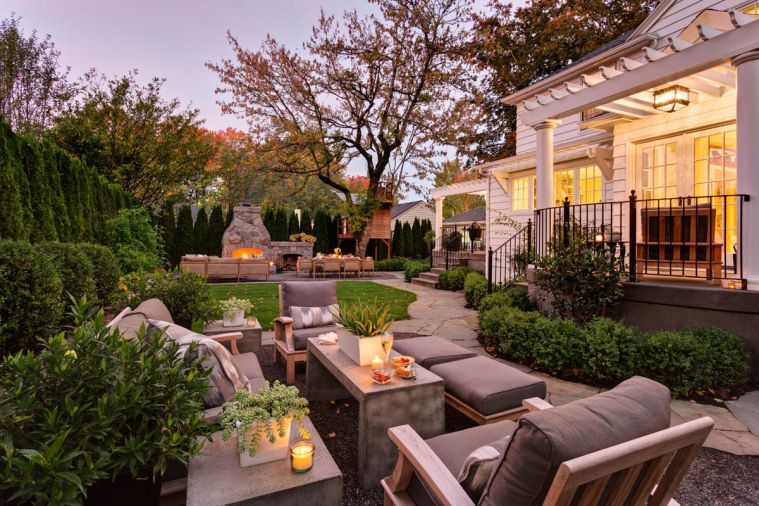 Pergola covered decks are a transition between inside and out in this Portland home. At ground level, a winding bluestone path connects the house to the outdoor rooms. The homeowners wanted the space to fulfill three roles: provide one area in which to entertain guests or gather with family, a second area with grassy lawn for sports practice and a third more intimate spot for reading or enjoying a quiet conversation. Furniture at the north end was custom designed for the space, while the Gloster loveseat, chairs and stools (pictured left) are from Fishels in Portland.