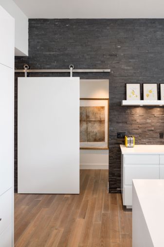 To bring the aesthetics of the outbuildings inside, Vanillawood installed a slab barn-style door to provide privacy between the home’s public and private spaces. Hung to slide across the hallway leading to the master bedroom and bath, the slab style door was treated with the same automotive finish as the cabinetry and hung from above on a track system with rollers from Krown Lab.