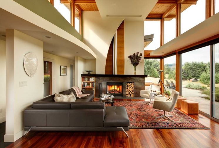 The curve of the dropped ceiling over the corridor mimics the curve on the fireplace wall. Both soften the straight lines of the windows and framing, the sharp angles of the roofline, and the structured furnishings. Besides the view, the fireplace is a beautiful part of the room. It is finished with anigre wood and a porcelain tile stained to look like brushed metal. The rug, purchased from Tufenkian Carpets, is the one traditional touch in the space.