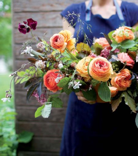 Eye-catching orange and chocolate tones highlight a bouquet of copper beech, black elderberry, ranunculus, sweet peas, grasses, mallow, nine bark, bronze fennel and snowberry foliage.