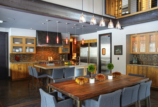 Tone and texture are repeated throughout the downstairs. Teak cabinetry brings warmth and pattern to the kitchen. The wood's orange hues reoccur in the backsplash and pendant lights, concrete is used in the floors and counters and echoed in the wall texture, and the color blue moves from walls to stools to chairs. Pendant lights above the dining table are hung high to allow an uninterrupted sight line from the kitchen to the great room.