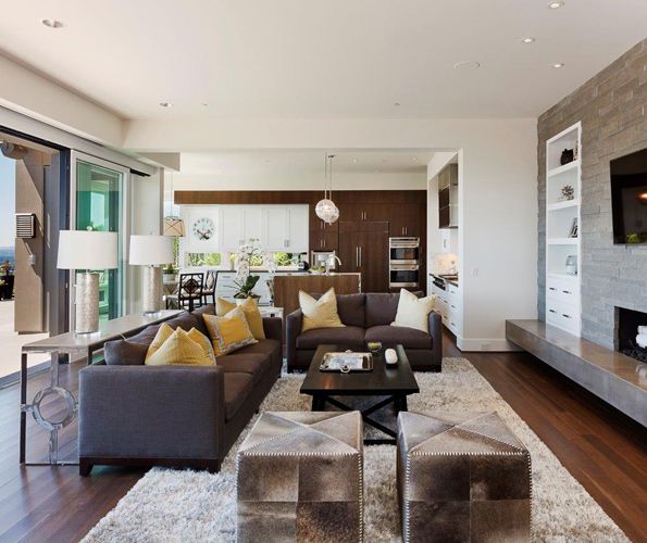 The Cenia Gray limestone fireplace inset with white shelving ties the living room to the adjacent kitchen in this open living area. A Bedford Brown 'Oh' sofa table continues the 'X' and 'O' theme. The fluffy silk rug defines the seating area, bordered by a pair of squared-off cowhide ottomans. The breakfast nook lighting, which features another 'X,' is from Visual Comfort. Antique chairs from Bedford Brown encircle the table.