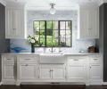 Dove White cabinets with Carrera marble countertops and backsplash are set against a Benjamin Moore Kendal Charcoal wall. A subway tile backsplash rises to enrobe restored steel casement windows. A family heirloom - 1970s blown glass Murano fruit bowl - lights up the counter near a Shaw farmhouse sink. Fully integrated dishwasher and recycling drawers are tucked behind recessed cabinetry below.