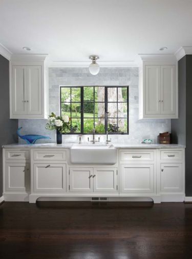 Dove White cabinets with Carrera marble countertops and backsplash are set against a Benjamin Moore Kendal Charcoal wall. A subway tile backsplash rises to enrobe restored steel casement windows. A family heirloom - 1970s blown glass Murano fruit bowl - lights up the counter near a Shaw farmhouse sink. Fully integrated dishwasher and recycling drawers are tucked behind recessed cabinetry below.